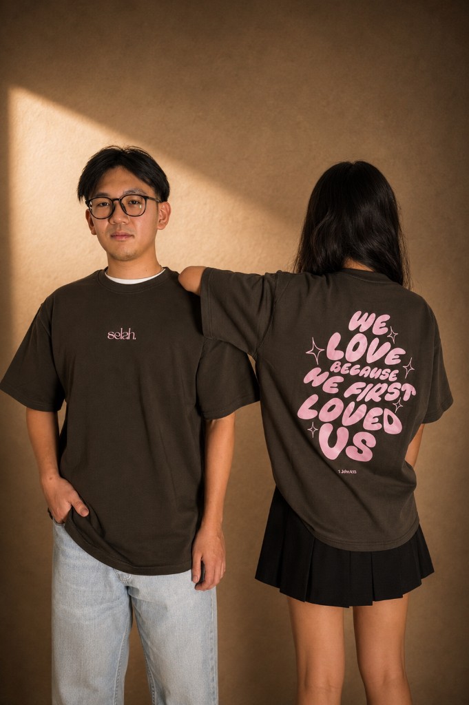 Dark brown Selah tee, "We love because He first loved us", 1 John 4:19